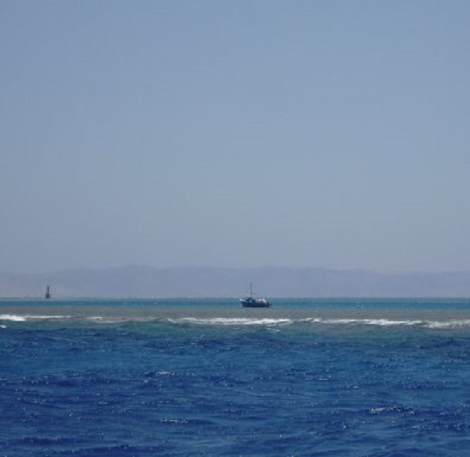 Vissersboot achter koraalrif. Op de achtergrond het ontoegankelijke eiland Shadwan