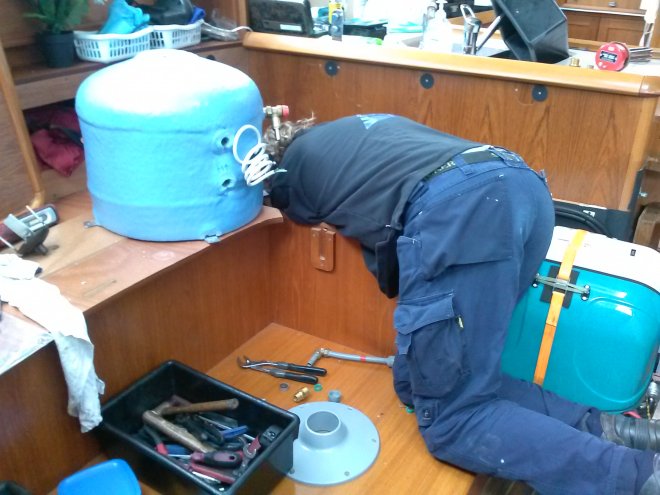 Fons bereidt de inbouw voor in een lastig hoekje van de nieuwe 40-liter warmwaterboiler. Dat is het bolle blauwe ding links, dat compleet in dat hoekje moet komen te staan. Helemaal rechts staat de generator.