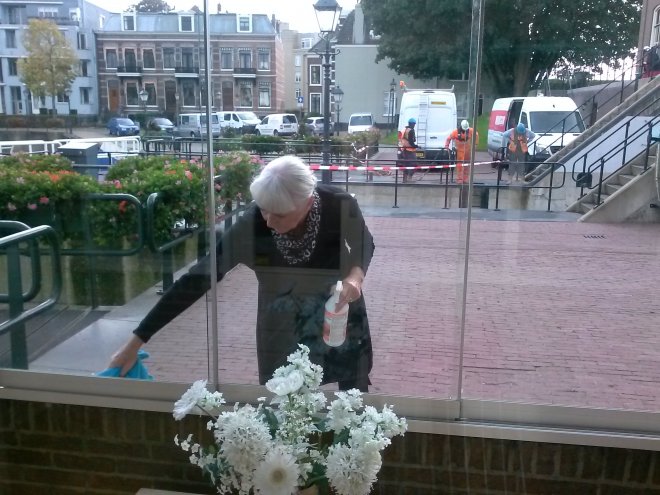 Ans spuit anti-ontgroeningsmiddel op het muurtje van de schuifpui. Achter haar is men bezig met onderhoud op de sluis.