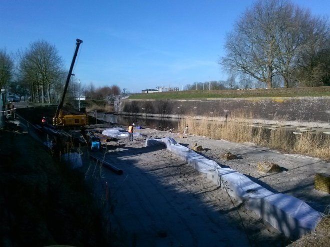 Bouwvakkers zijn bezig met heien voor het afzichtelijke hotel aan de Duveltjesgracht. De middeleeuwse muur- en torenresten zijn ingepakt met plasticfolie.